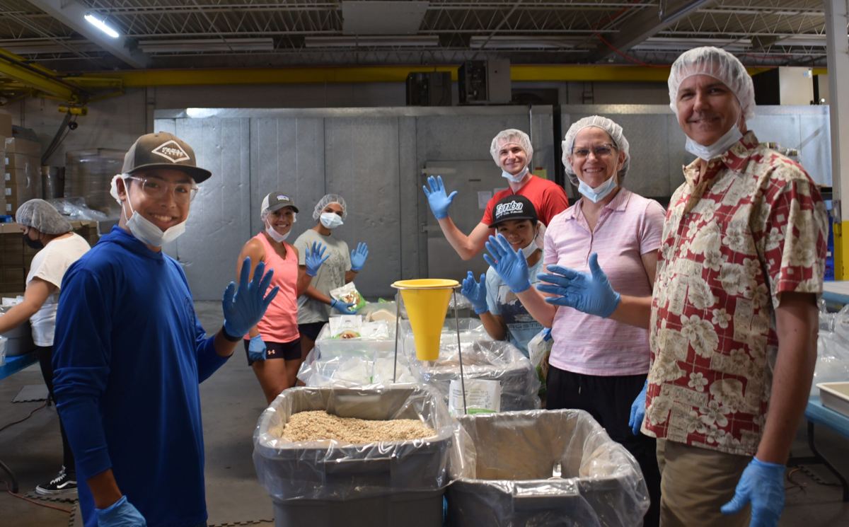 Group of volunteers waving at a Colorado Feeding Kids packing event