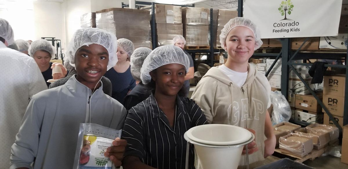 Teen volunteers packing meals together at the Colorado Feeding Kids warehouse
